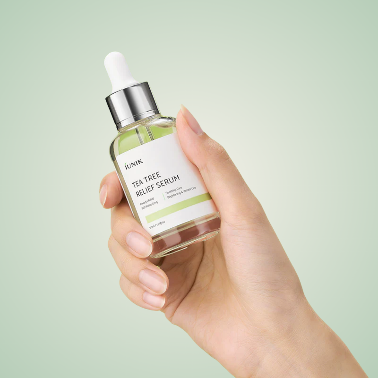 Hand holding iUNIK Tea Tree Relief Serum 50ml with silver dropper cap