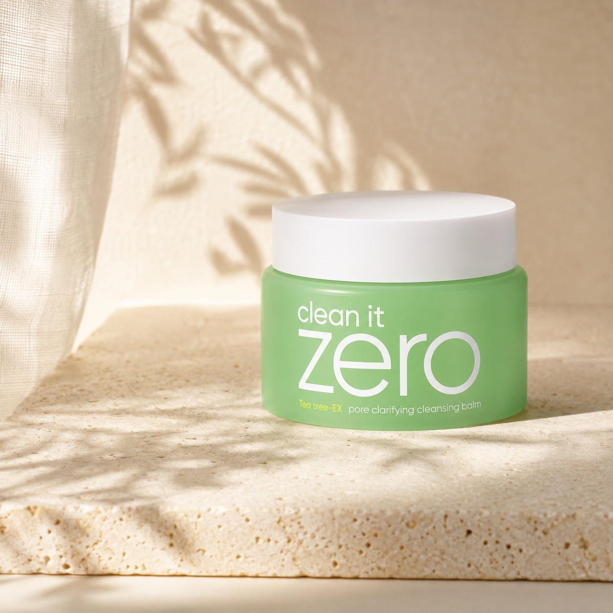 Banila Co Clean It Zero Tea Tree-EX Pore Clarifying Cleansing Balm displayed on warm travertine with soft morning light in a premium Korean skincare hero photo.