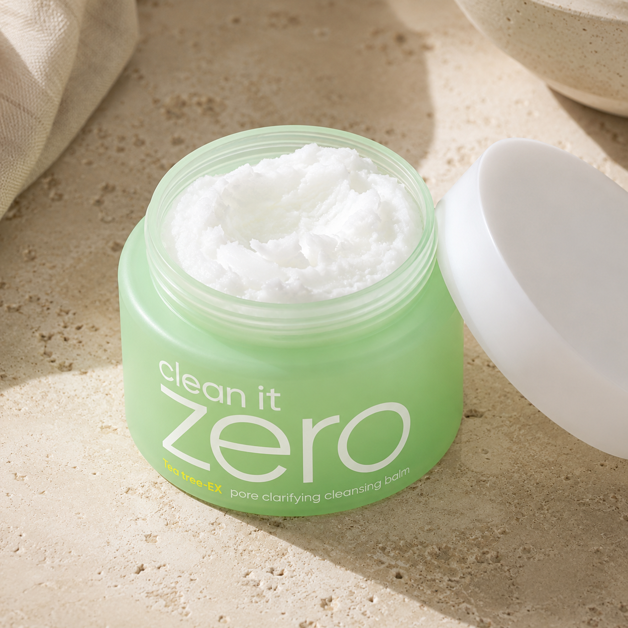 Banila Co Clean It Zero Tea Tree-EX Pore Clarifying Cleansing Balm styled on a warm travertine vanity with linen, ceramic, and soft botanical shadows.