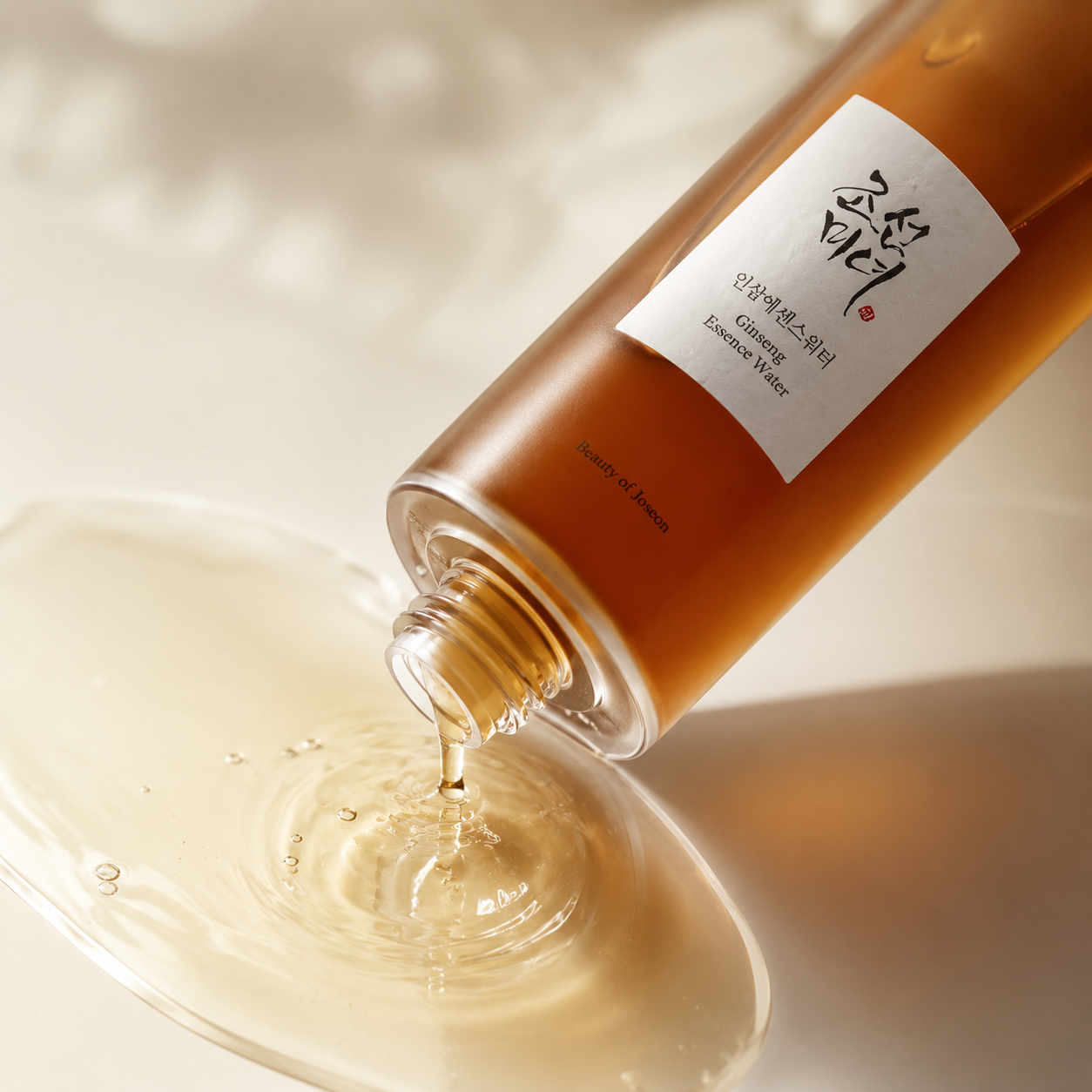 Beauty of Joseon Ginseng Essence Water 150ml shown pouring amber essence onto a smooth surface, highlighting its lightweight watery texture.