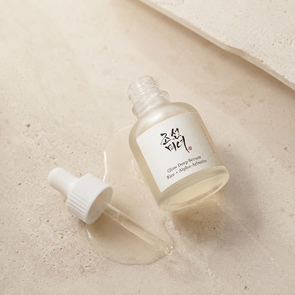Beauty of Joseon Glow Deep Serum Rice + Alpha-Arbutin 30ml shown open with the dropper beside the bottle on warm travertine.