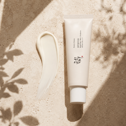 Beauty of Joseon Relief Sun Rice + Probiotics SPF50+ PA++++ 50ml beside a smooth white sunscreen cream texture on warm travertine, showing its lightweight creamy finish in soft natural light.