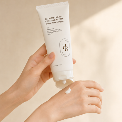 Heveblue Salmon Caring Centella Cream 100ml being applied onto the hand in soft natural light, showing the creamy texture in a calm Korean skincare routine moment.