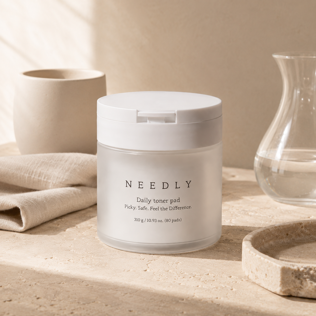 Needly Daily Toner Pad 310g 80 pads shown open with textured toner pads and clear tweezers on warm travertine in a premium skincare editorial photo.
