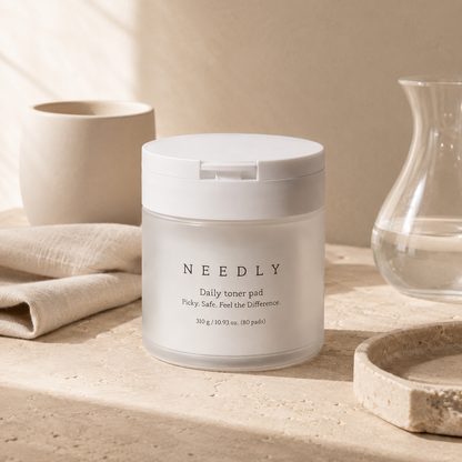 Needly Daily Toner Pad 310g 80 pads shown open with textured toner pads and clear tweezers on warm travertine in a premium skincare editorial photo.