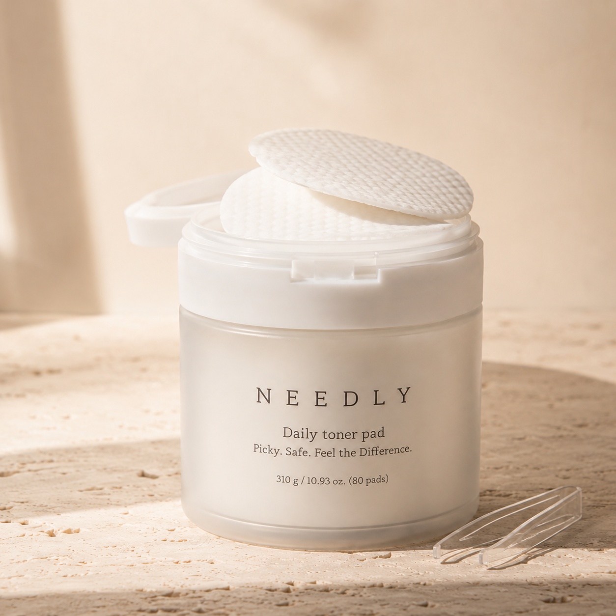 Needly Daily Toner Pad 310g 80 pads styled on a warm travertine vanity with beige linen, ceramic cup, glass vessel, and soft natural light