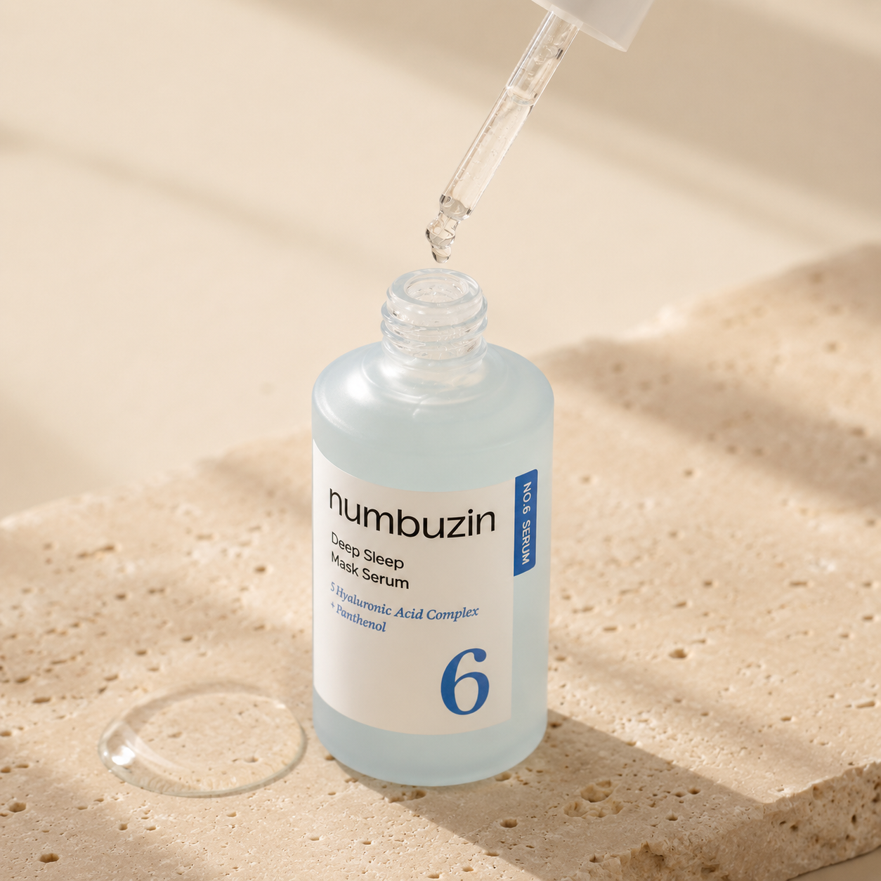 Numbuzin No.6 Deep Sleep Mask Serum 50ml shown open with a glass dropper dispensing clear hydrating serum above the bottle on warm travertine.