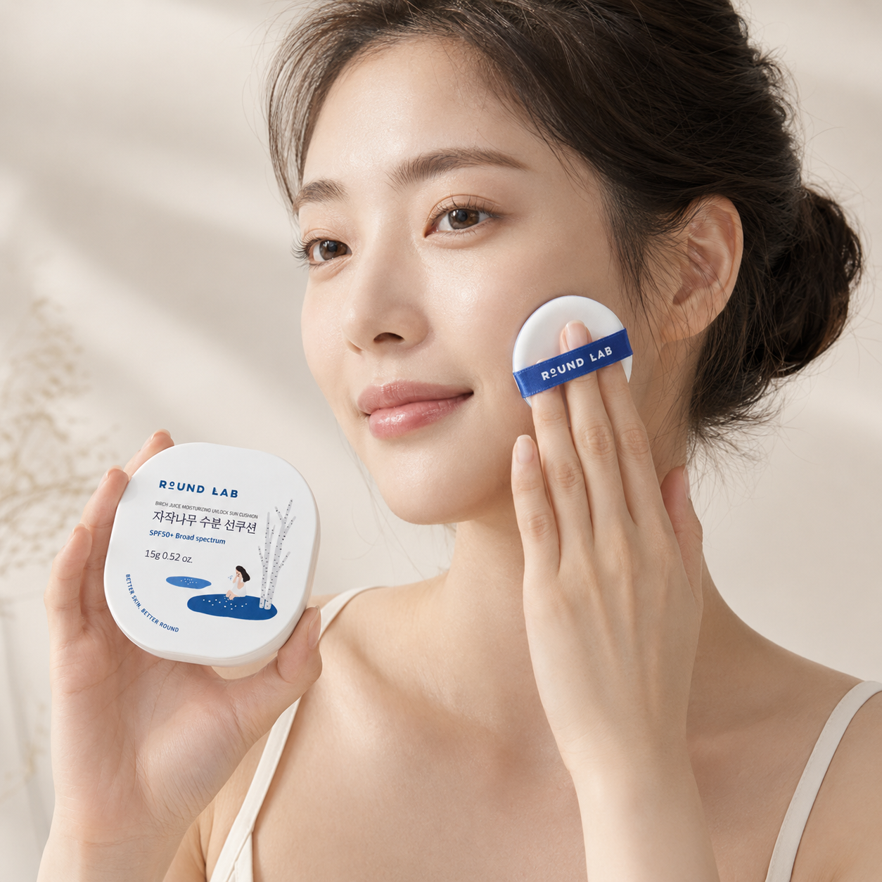 Round Lab Birch Juice Moisturizing UVlock Sun Cushion SPF50+ being applied to the cheek with the puff in a clean Korean skincare application photo.