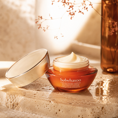 Sulwhasoo Concentrated Ginseng Rejuvenating Cream shown open with a rich cream swirl on warm travertine in a premium skincare texture photo.