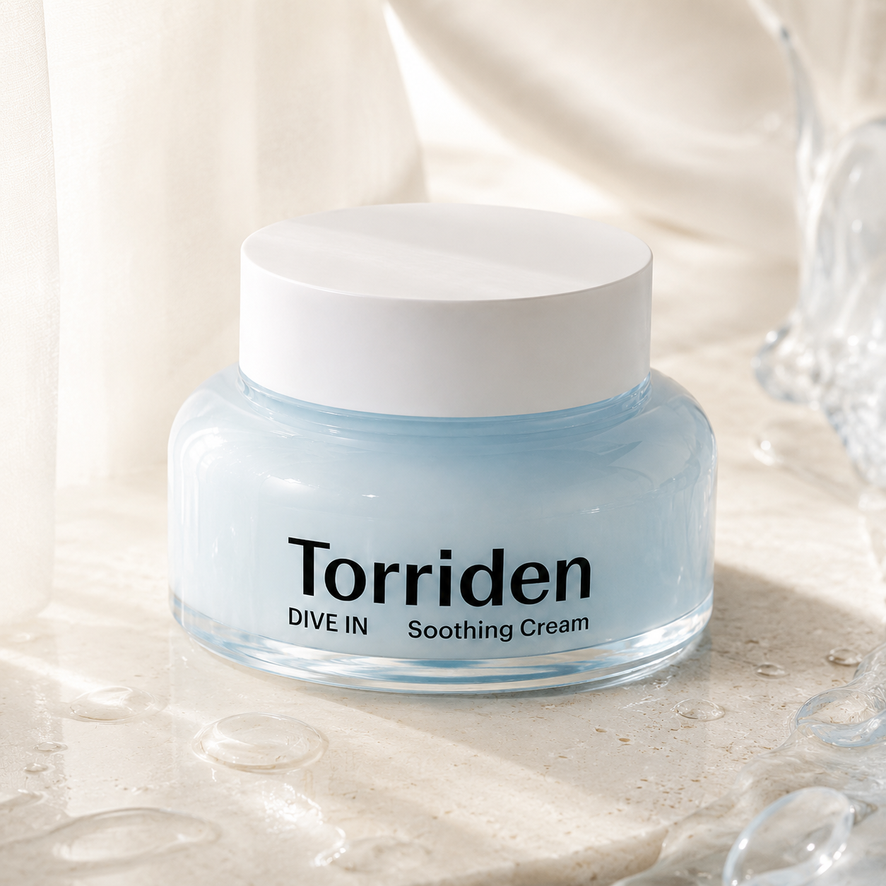 Torriden Dive-In Hyaluronic Acid Soothing Cream 100ml styled on a warm travertine vanity with beige linen, ceramic cup, and glass vessel in soft natural light