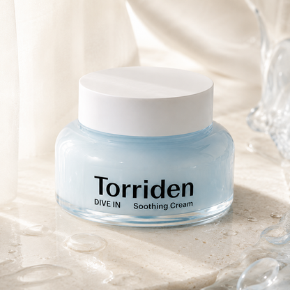 Torriden Dive-In Hyaluronic Acid Soothing Cream 100ml styled on a warm travertine vanity with beige linen, ceramic cup, and glass vessel in soft natural light